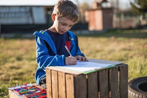 Little boy writing and learning in the garden bicouse school is closed due to Covid-19 pandemic in