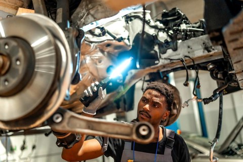 Young mechanic using flashlight inspecting car chassis and suspension in a professional auto repair