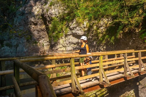 Mother and child wearing helmets are walking on a wooden bridge, enjoying the natural beauty of