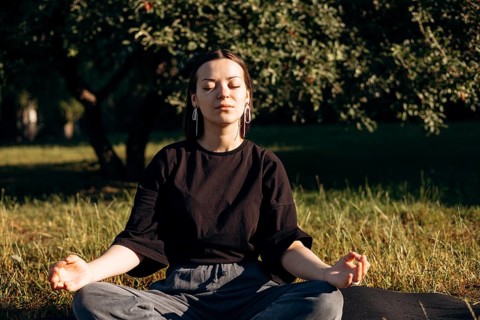 A teenage girl meditates in a serene garden during the morning, eyes closed and relaxed. Sunlight