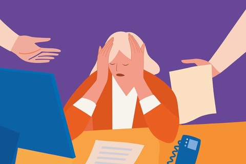 An overwhelmed and stressed worker at her desk, hands on head as her colleagues hand her documents
