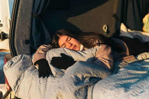 A young Latina woman sleeps soundly, wrapped in a cozy blanket in a van while camping in Iceland.
