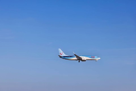 Passenger airplane from the travel company Tui with tourists to a resort flying on a blue sky,
