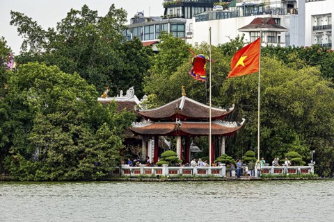 Traditional temple in Vietnam by the lake with trees in the background, Vietnamese flag waving, The