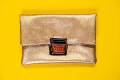 Golden faux leather clutch against a plain yellow background