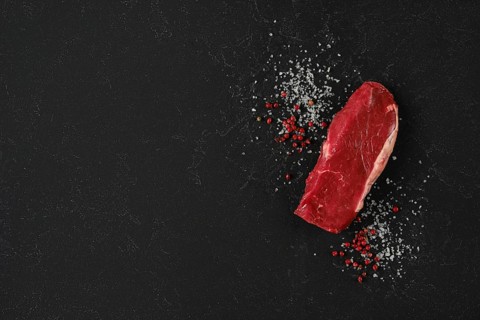 A piece of fresh raw beef sirloin steak on a dark countertop surrounded by coarse sea salt and red