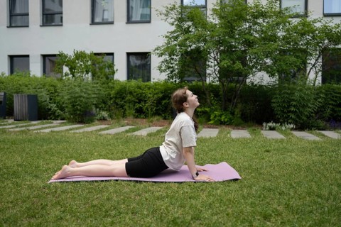 A teen girl performs a yoga pose on a purple mat in a green backyard, focusing on relaxation and