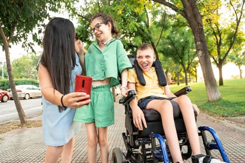 A joyful family enjoys a sunny day at the park. The girl with a tracheostomy smiles as her brother