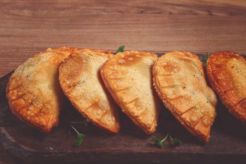 Fried chebureks, deep-fried, mini, on a chopping board, wooden table, close-up, no people