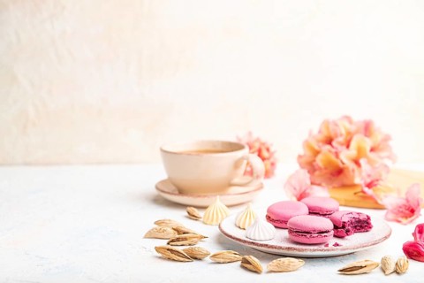Purple macarons or macaroons cakes with cup of coffee on a white concrete background decorated with