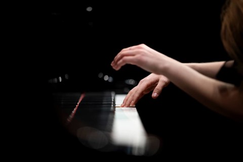 Hands and arms of a young pianist playing on the keyboard of a Steinway & Sons grand piano,