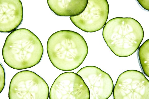 Slices of fresh cucumber are arranged on a light background, showcasing their crisp texture and