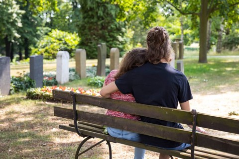 Young couple sitting on a bench between graves, Riesa Cemetery, Saxony, Germany