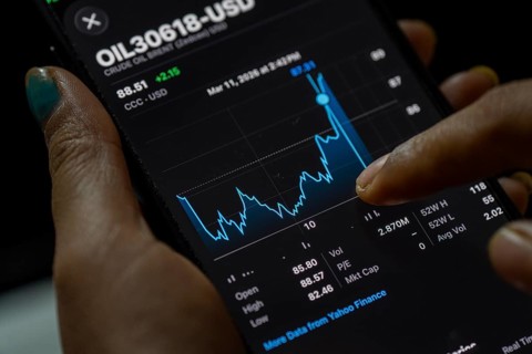 In this photo illustration, a person looks at a smartphone displaying Brent crude oil prices in