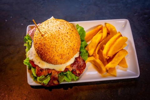Hamburger with bacon and french fries on a black background, on a white plate