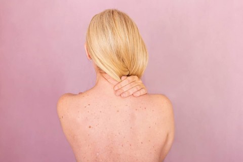 A woman with blonde hair is featured from the back against a pink background, highlighting skin