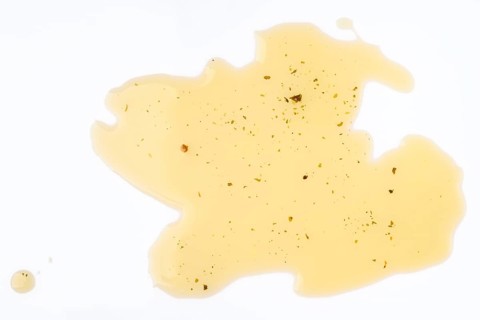 Spilled Olive oil with herbs with specks on a white background showcasing intriguing textures and