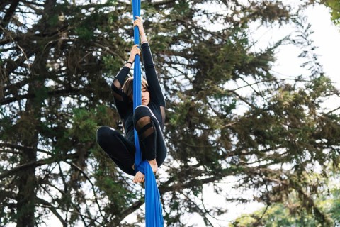 Aerial artist performing acrobatics on blue fabric against a natural backdrop in a Bogota park The