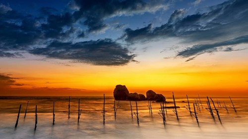 Wooden posts in the sea at sunset with dramatic clouds and orange sky, The Stilt Fishermen's Beach