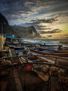Fishing boats along a rocky stretch of coast at sunset with dramatic clouds, romantic harbor scene,