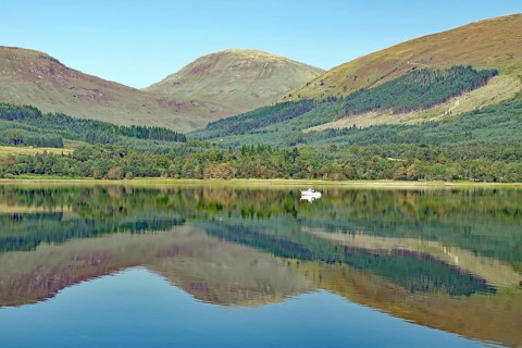 A quiet spur of an estuary with reflections of surrounding mountains and forests on a clear day,