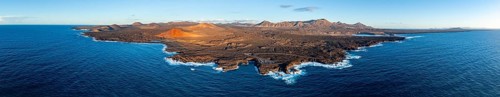Coast with lava fields, volcanic landscape near Los Hervideros with red volcano Montaña Bermeja, in