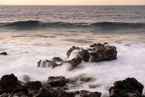 Surf with waves crashing over black lava rocks on the coast, Pacific Ocean at dusk, Easter Island