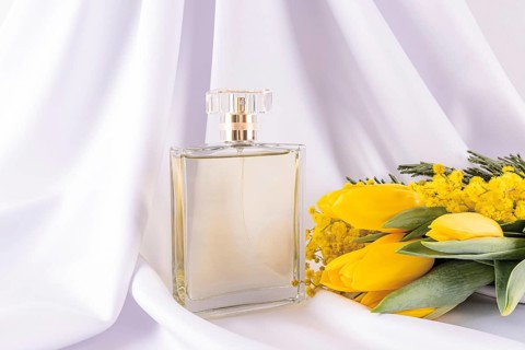 A glass perfume bottle with a gold cap sits elegantly on white fabric, accompanied by vibrant