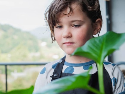 A close-up portrait of a contemplative young girl indoors, gazing past a fresh green leaf,