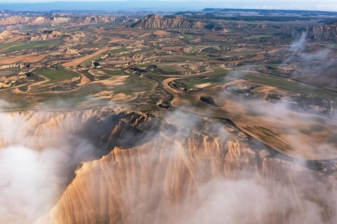 A stunning aerial view reveals a craggy landscape interspersed with lush fields Mist cloaks the