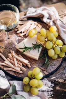 A serene outdoor still life featuring a glass of wine, green grapes, rosemary and cheese on a