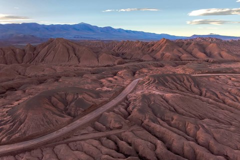 An aerial view of a rugged desert mountain landscape at sunrise, showcasing intricate patterns and