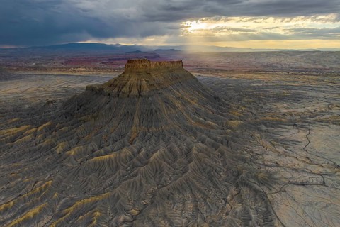 A dramatic view of Factory Butte as the sunset casts golden highlights across its rugged terrain,