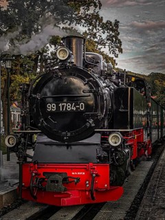 Old, historic steam locomotive in bright colors on tracks at the station in a nostalgic atmosphere,