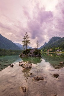 Hintersee with rocks and trees in the foreground, surrounded by mountains after sunset with
