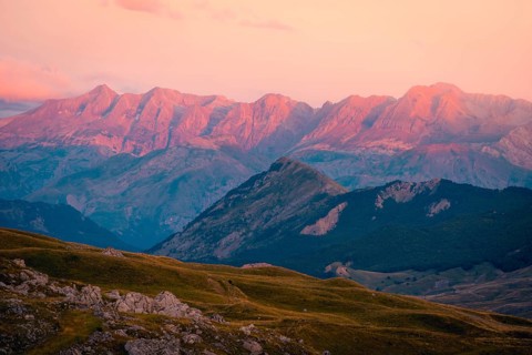 A stunning mountain range illuminated by the soft glow of sunset, featuring vibrant pink and orange