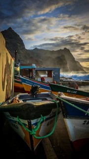 Colorful fishing boats on the shore with ropes and setting sun over the sea, dramatic coastal