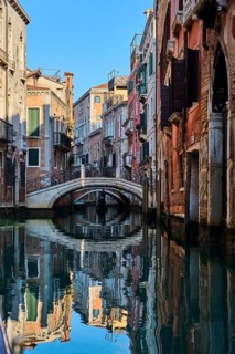 View from a gondola on a waterway in Venice going through the houses on a quiet and sunny morning