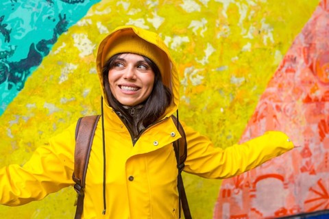 Young woman smiling while wearing a yellow raincoat and beanie, exploring a vibrant urban street