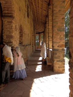 Sunlit corridor with traditionally dressed people and stone walls, Debre Birhan Selassie Church,