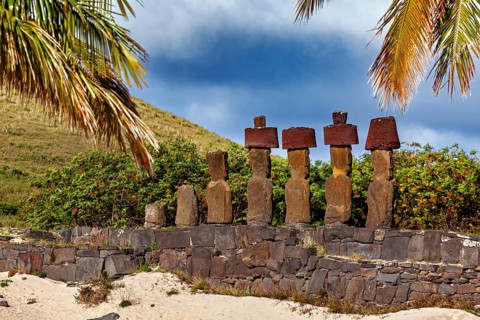 The Moai statues rise amidst palm trees and vegetation on Easter Island, under an overcast sky, The