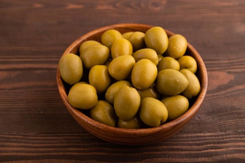 Fresh green olives in wooden bowl on brown wooden background. side view, close up
