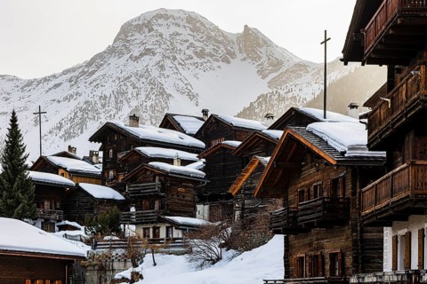 Snow-covered old farmhouses, large wooden cross, historic town center, in the back the snow-capped