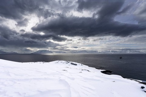 Snow-covered coastal landscape with expedition participants and anchoring ship against a dramatic