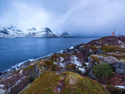 Small lighthouse at the end of Husøy island with a view across the fjord to the sea, Senja island,
