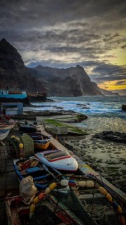 Fishing boats along a rocky coast at sunset with dramatic clouds, romantic harbor scene, Ponta do