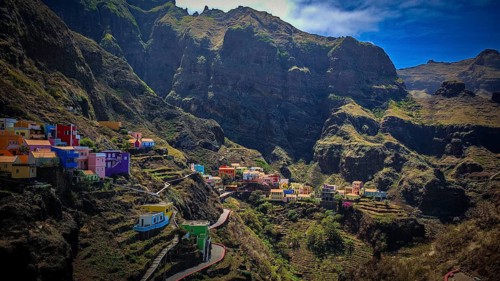Panoramic view, small settlement, colorful village, nestled in raw, dramatic mountains under blue