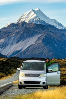 A woman stands beside her parked car, enjoying the stunning autumn view of Mount Cook in New