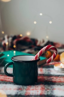 Green mug with a steaming beverage and a classic candy cane, set against a festive, softly lit