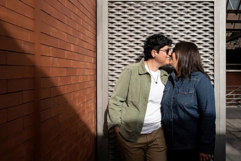 A joyful lesbian couple shares a tender moment outdoors against a brick wall. Both women are